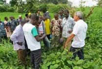 Instructor in a white shirt talking to a group of men gathered at the edge of a green field.