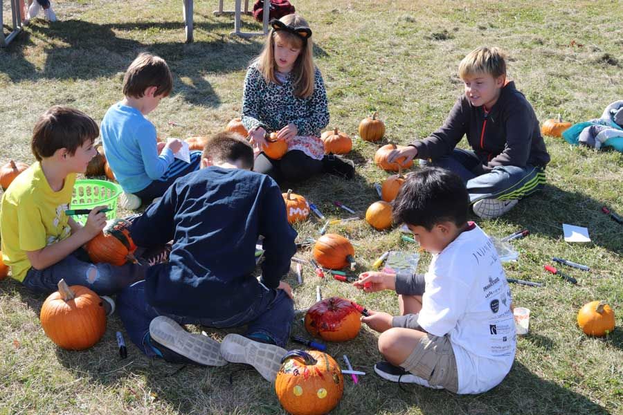 Group of children sitting in the grass decorating pumpkins together with markers