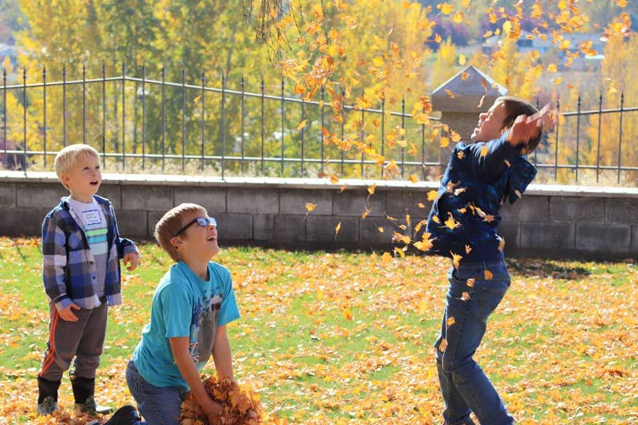 Boy tossing a handful of fall leaves into the air while friends watch and laugh