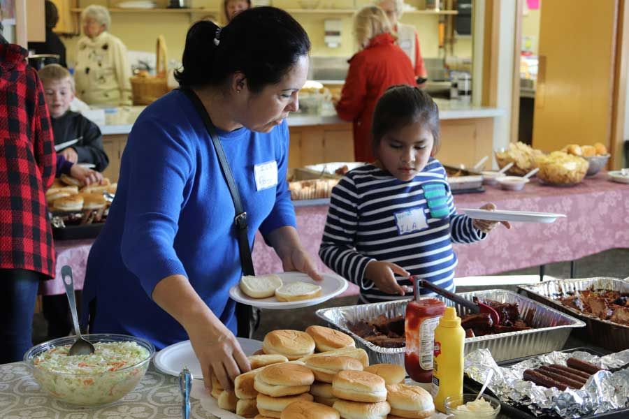 Volunteers serving hamburger buns, ribs, and barbecue sides on the food line at the community lunch