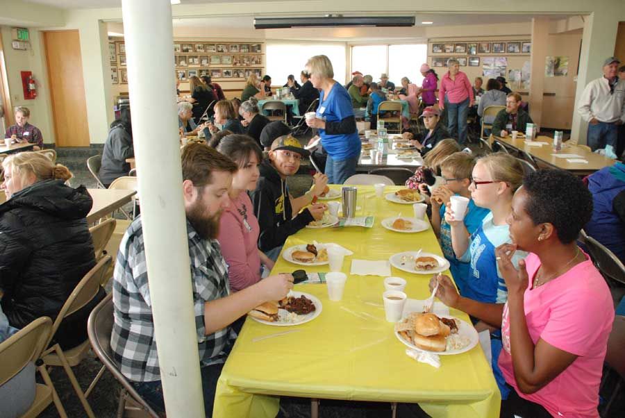 Families and volunteers sitting together at long tables eating lunch at the harvest festival
