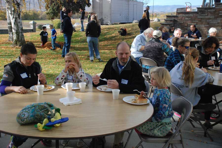 Families and children eating lunch together at outdoor tables during the fall harvest event