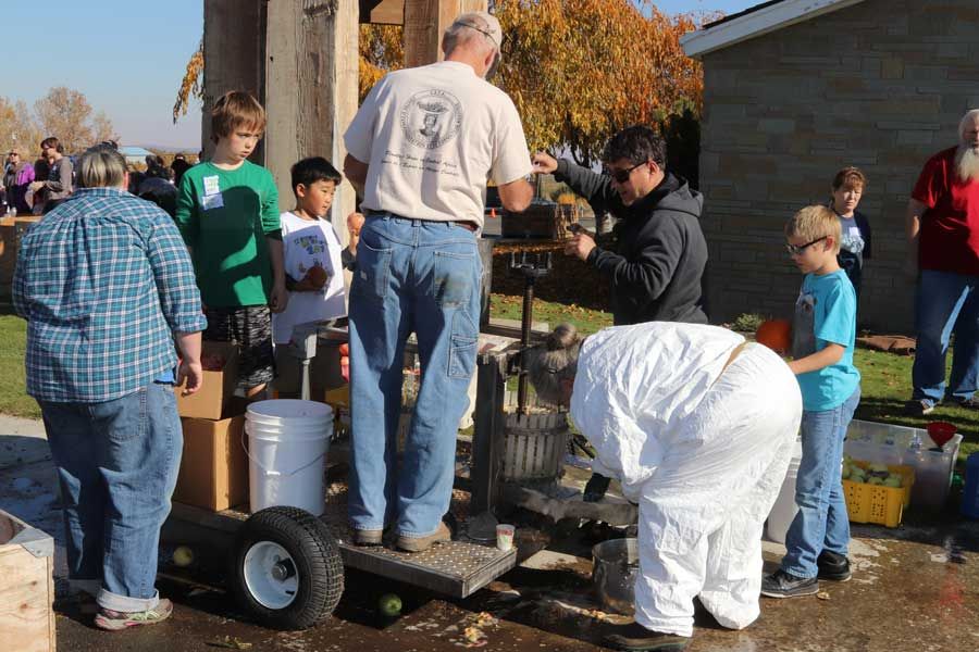 Volunteers and children gathered around a mobile apple cider press operating outdoors