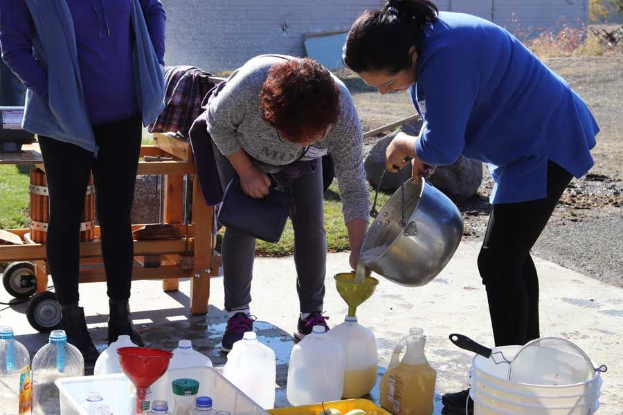 Volunteers pouring fresh pressed apple cider into jugs and bottles through funnels