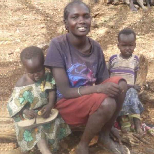 Woman sitting on a log outdoors with a small child on either side of her, smiling towards the camera.